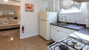 Una cocina compacta con estufa a gas, armarios blancos, un refrigerador y una ventana con persianas.