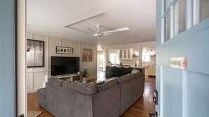 Una sala de estar moderna con un sofá seccional gris, un televisor de pantalla plana y un ventilador de techo.