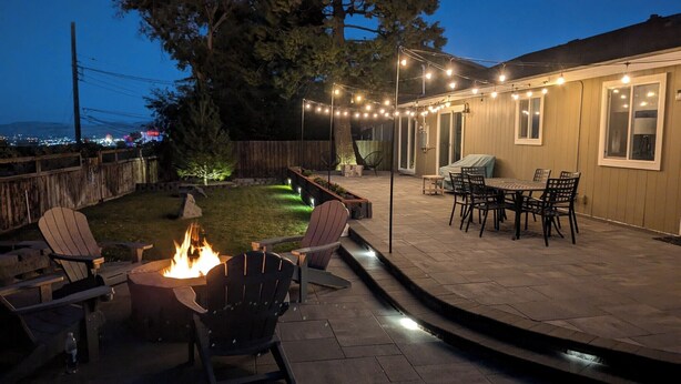 Un patio con fogón, mobiliario exterior e iluminación con luces colgantes.