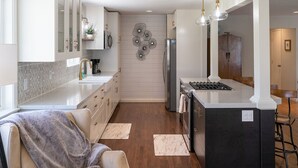 Una cocina moderna con armarios blancos, una isla con encimera de mármol, electrodomésticos de acero inoxidable e iluminación colgante.