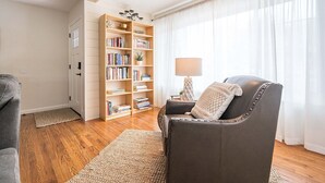 Una sala de estar con un sillón de cuero, una estantería, una lámpara y un ventanal con cortinas traslúcidas.