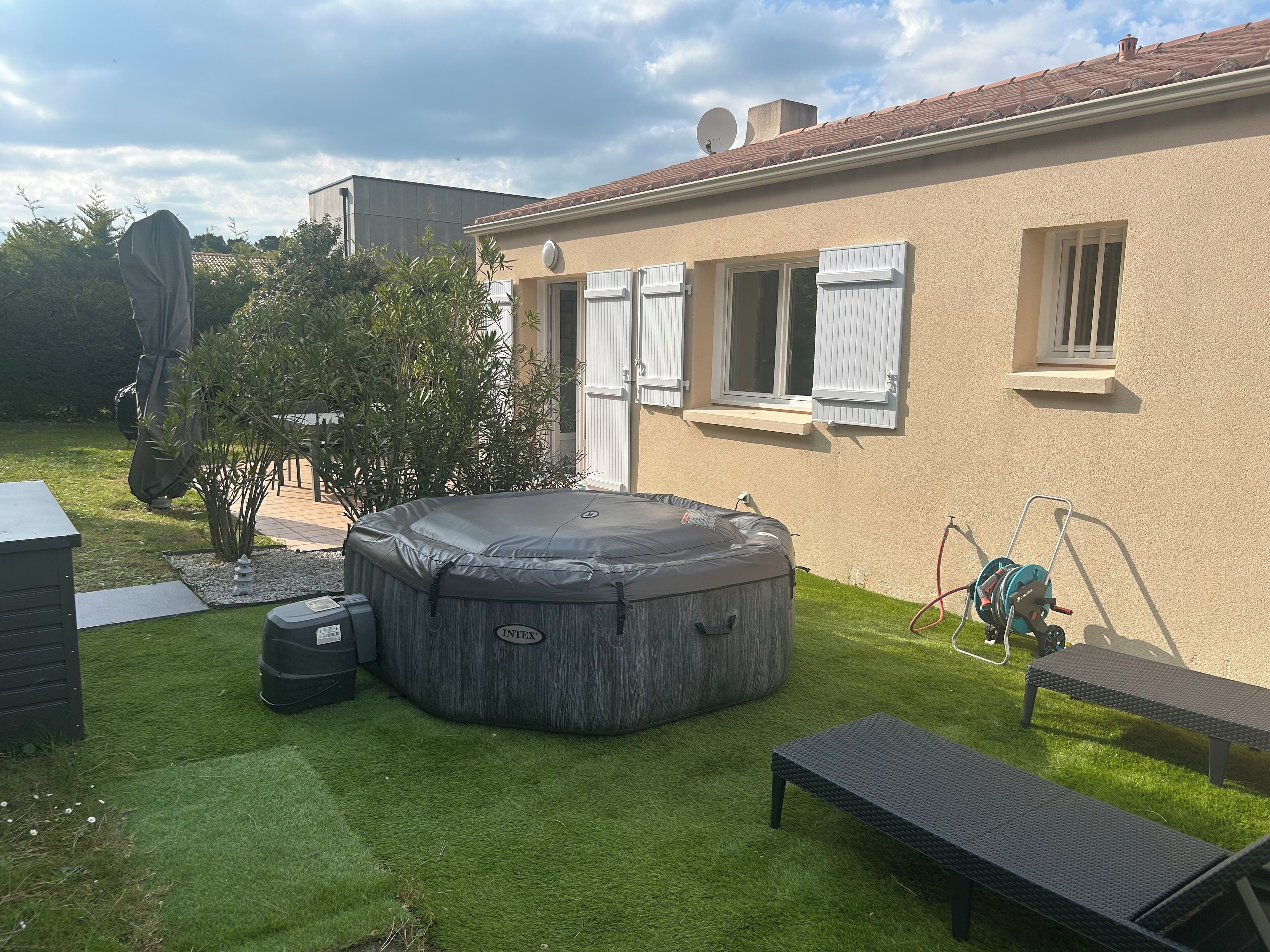 A backyard with a hot tub, a covered table, and a small deck.