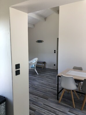 A modern room with a wooden floor, a white wall, a white chair, a wooden table, and a ceiling vent.
