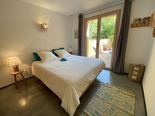 A bedroom with a bed, a lamp, a wall clock, and a view of the outdoors.