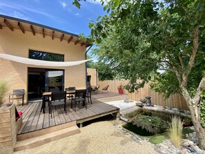 A patio with a wooden deck, outdoor furniture, a small pond with lily pads, and a wooden fence.