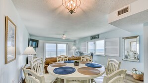 A dining area with a round table, white chairs, and blue placemats. - Direct Ocean- Wrap Around Balcony (Indialantic)
