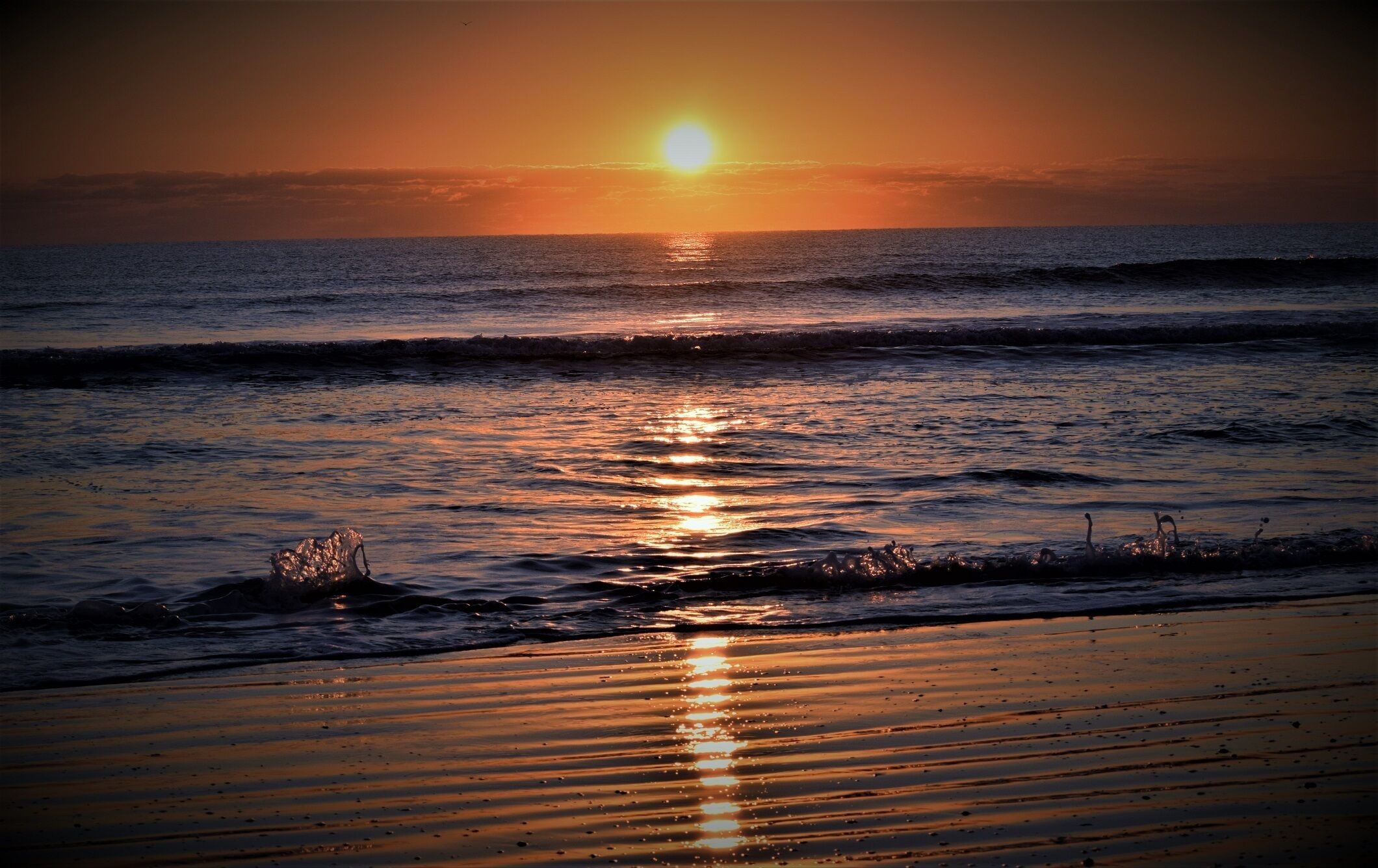Atardecer sobre una playa con olas que reflejan la luz del sol.