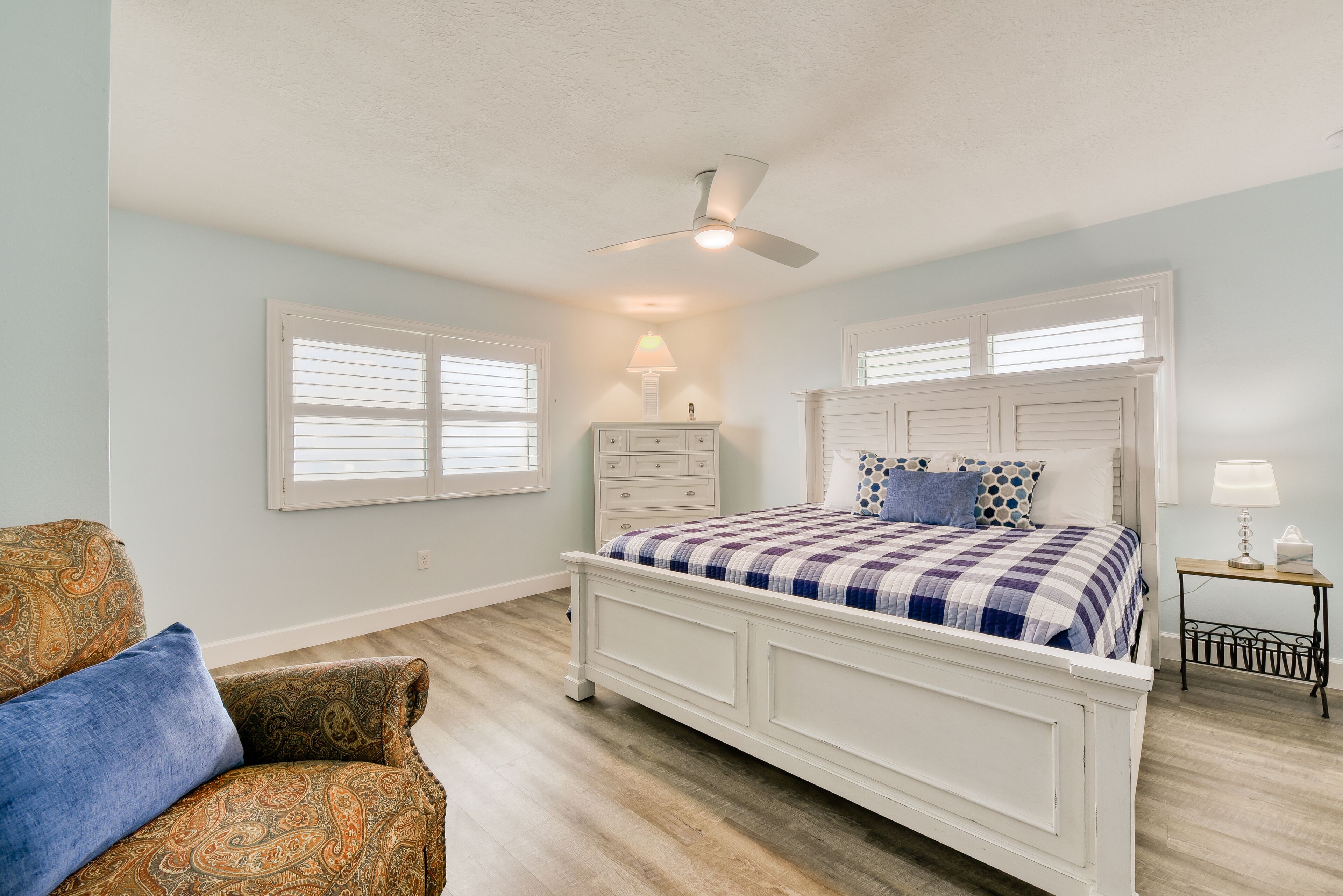A bedroom with a bed, a chair, a nightstand, and a ceiling fan.