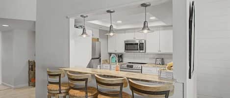 A modern kitchen with white cabinets, a central island with bar stools, and pendant lighting.
