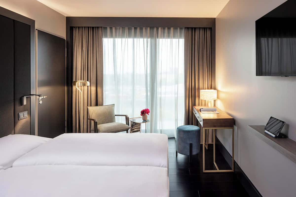Ein Hotelzimmer mit einem großen Bett, einem Schreibtisch mit Lampe, einem Sessel und einem kleinen Tisch mit Blumen.