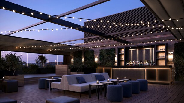 An outdoor seating area with a bar, wooden deck, and string lights. - Hotel AMANO East Side (Berlin)
