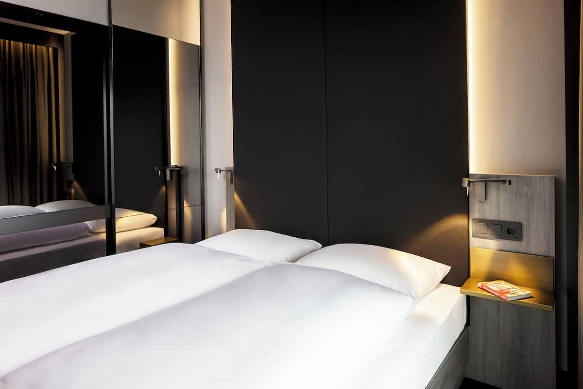 Ein modernes Hotelzimmer mit einem großen Bett, einem Nachttisch mit einem Buch und einem Kleiderschrank.
