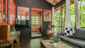 Interior acogedor de una cabaña con piso de madera, un sofá, un sillón mecedor y un televisor.