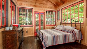 Un dormitorio de cabaña de madera con una cama, un aparador y ventanas amplias.