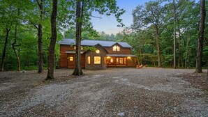 A wooden cabin with a stone foundation, surrounded by a gravel driveway, set in a forested area. - Blue Pine Divine - 1+ Bedrooms, 2 Baths, Sleeps 6, pet friendly, Hot Tub (Broken Bow)