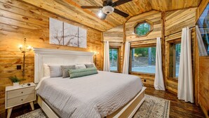 A wooden cabin bedroom with a bed, nightstand, and a ceiling fan. - Blue Pine Divine - 1+ Bedrooms, 2 Baths, Sleeps 6, pet friendly, Hot Tub (Broken Bow)