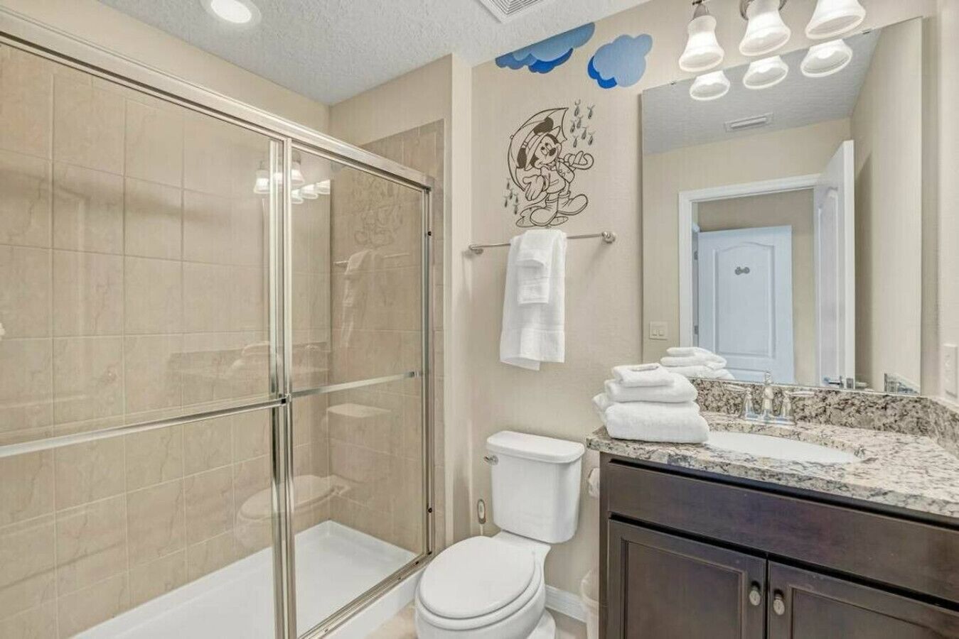 Une salle de bain moderne avec une douche à parois de verre, des toilettes blanches, un lavabo en marbre et un grand miroir.