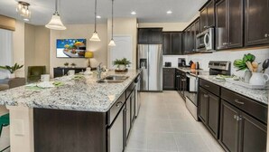 A modern kitchen with dark cabinetry, a granite countertop, stainless steel appliances, pendant lighting, and a large island with a sink. - Themed rooms - Resort acess (Kissimmee)