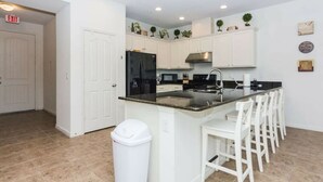 A modern kitchen with white cabinetry, a black refrigerator, and a bar area with white chairs. - Great Lake View - Pet Friendly (Kissimmee)