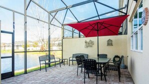 A covered patio with brick flooring, black metal chairs, a table, and a red umbrella. - Great Lake View - Pet Friendly (Kissimmee)