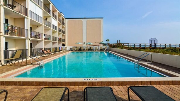Une piscine entourée d’un bâtiment doté de balcons, avec des chaises longues et des parasols à proximité.