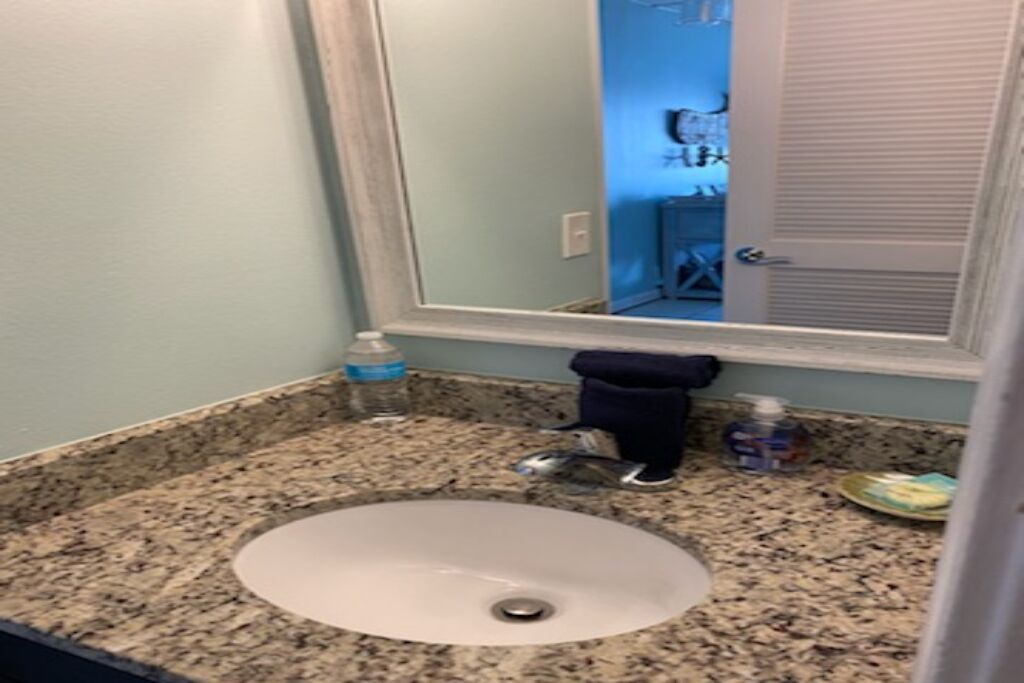 Casa de banho com bancada de granito, lavatório branco, espelho e suporte para toalhas.