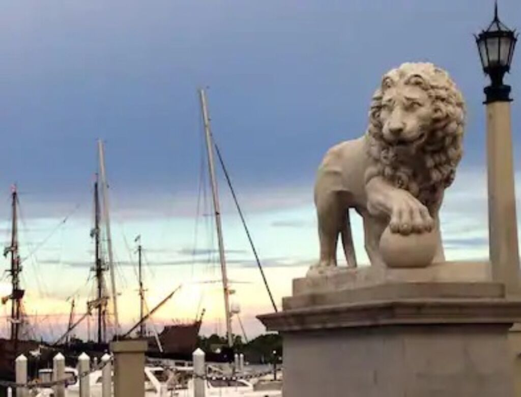 A lion statue at a harbor with boats in the background.