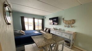 Une pièce de taille modeste comprenant un lit, une petite table, un téléviseur et une étagère fixée au mur.