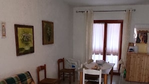Uma sala de estar com sofá, cadeiras, uma mesa de jantar e uma janela com cortinas.