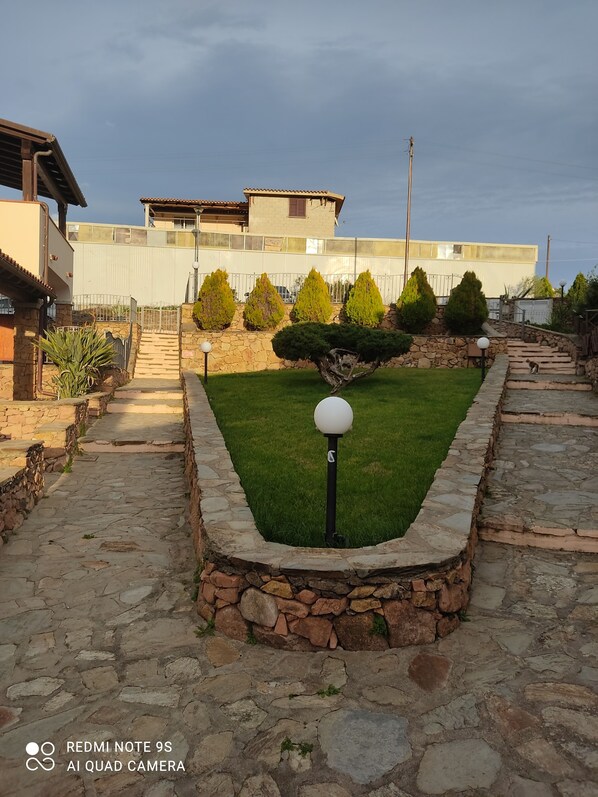 A stone pathway leading to a house with a stone wall and a small lawn. - townhouse (Limpiddu)