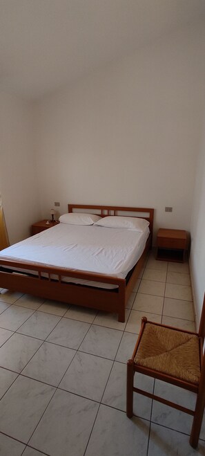 A bedroom with a wooden bed, a nightstand, a chair, and tiled flooring. - townhouse (Limpiddu)
