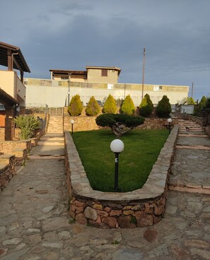 A stone pathway leading to a house with a stone wall and a small lawn. - townhouse (Limpiddu)