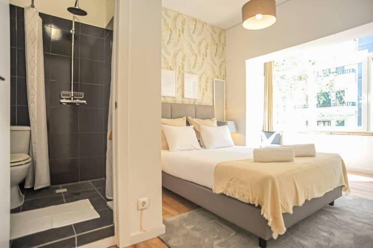 Une chambre avec un lit, une douche et une fenêtre donnant sur des immeubles.