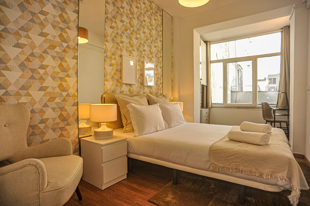 Une chambre d’hôtel avec un lit, une chaise, une table de chevet et une grande fenêtre.