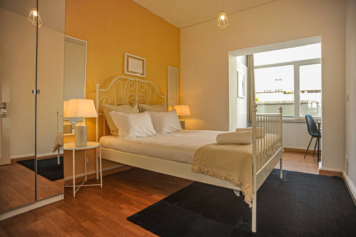 Une chambre à coucher avec un lit, des tables de chevet, une fenêtre et une vue sur l’extérieur.