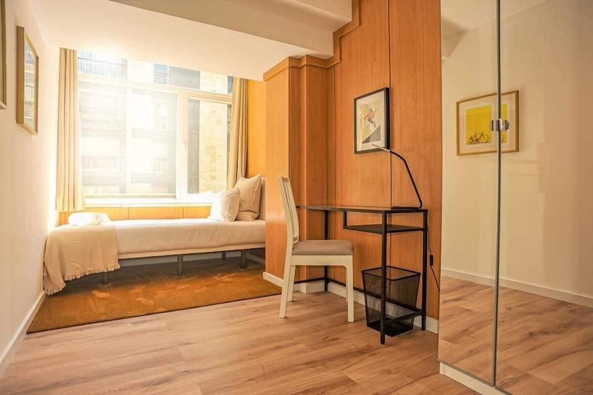 Une pièce avec un lit, une chaise, une petite table et une fenêtre.