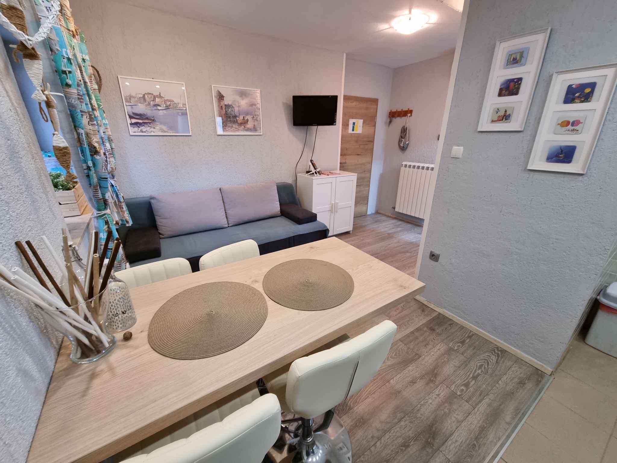 A dining area with a wooden table, white chairs, and a TV mounted on the wall.