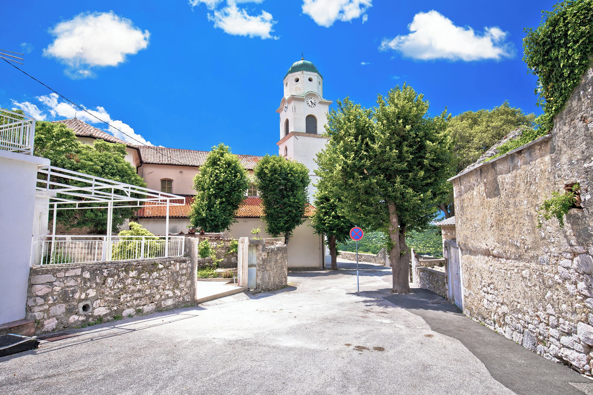 A narrow street with a stone wall on one side and a building with a clock tower on the other.