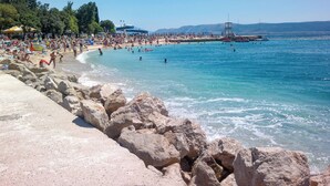 Une plage au rivage rocheux, avec une eau d’un bleu limpide, où l’on peut voir des gens nager et prendre des bains de soleil.