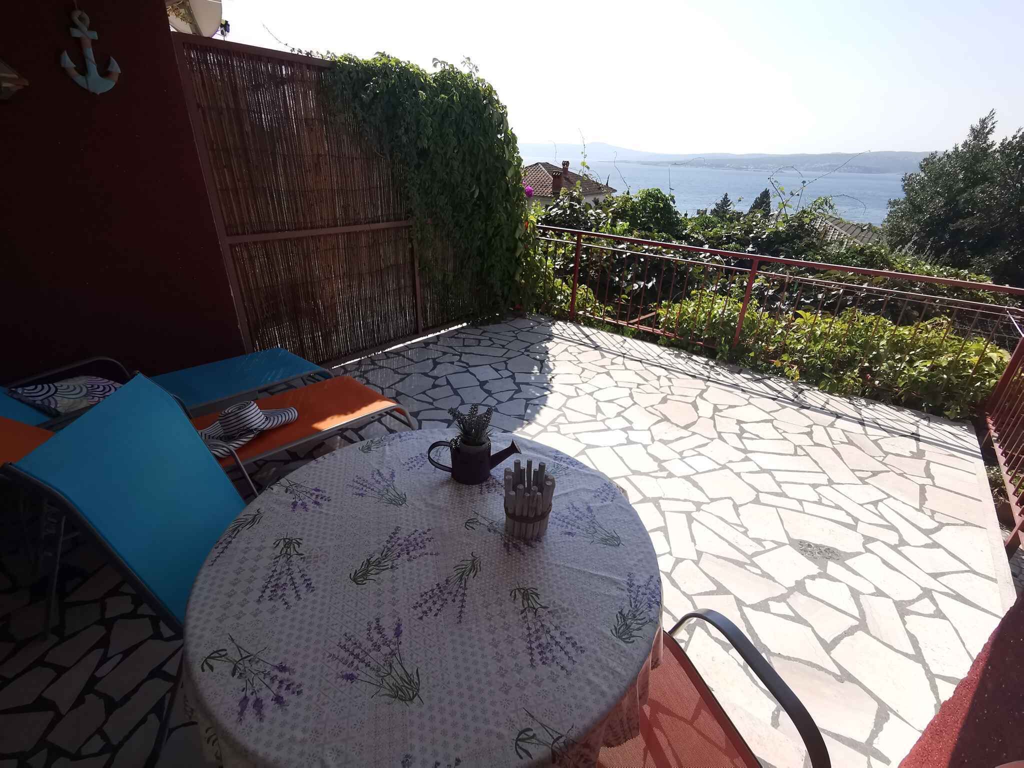 En terrasse med et rundt bord, stole og havudsigt.