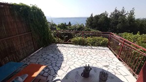 Een terras met een stenen vloer, een tafel met een tafelkleed met bloemenmotief en uitzicht op zee.