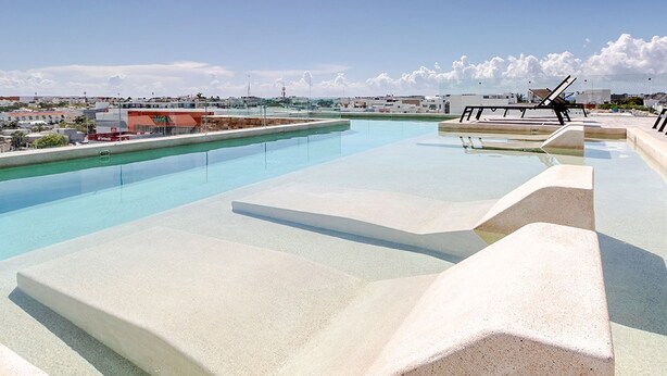 A rooftop infinity pool with clear blue water, a view of the cityscape, and a lounge area with sun loungers. - Veranto (Playa del Carmen)