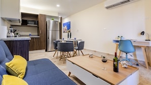 A modern living room with a blue sofa, a wooden coffee table, and a dining area with chairs and a table. - Veranto (Playa del Carmen)