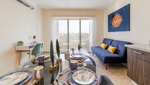 A modern living room with a dining area, a sofa, and a city view through large windows. - Veranto (Playa del Carmen)