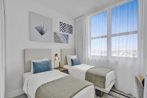 Habitación de hotel con dos camas, un ventanal con vistas y decoración en la pared.