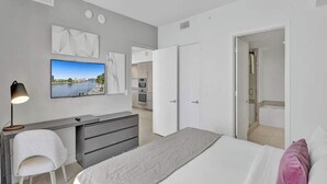 A modern bedroom with a bed, a desk, a TV, and a bathroom visible through an open door. - Enjoy the perfect blend of comfort, elegance, and luxury in this stunning 3-bedroom apartment (Hollywood)