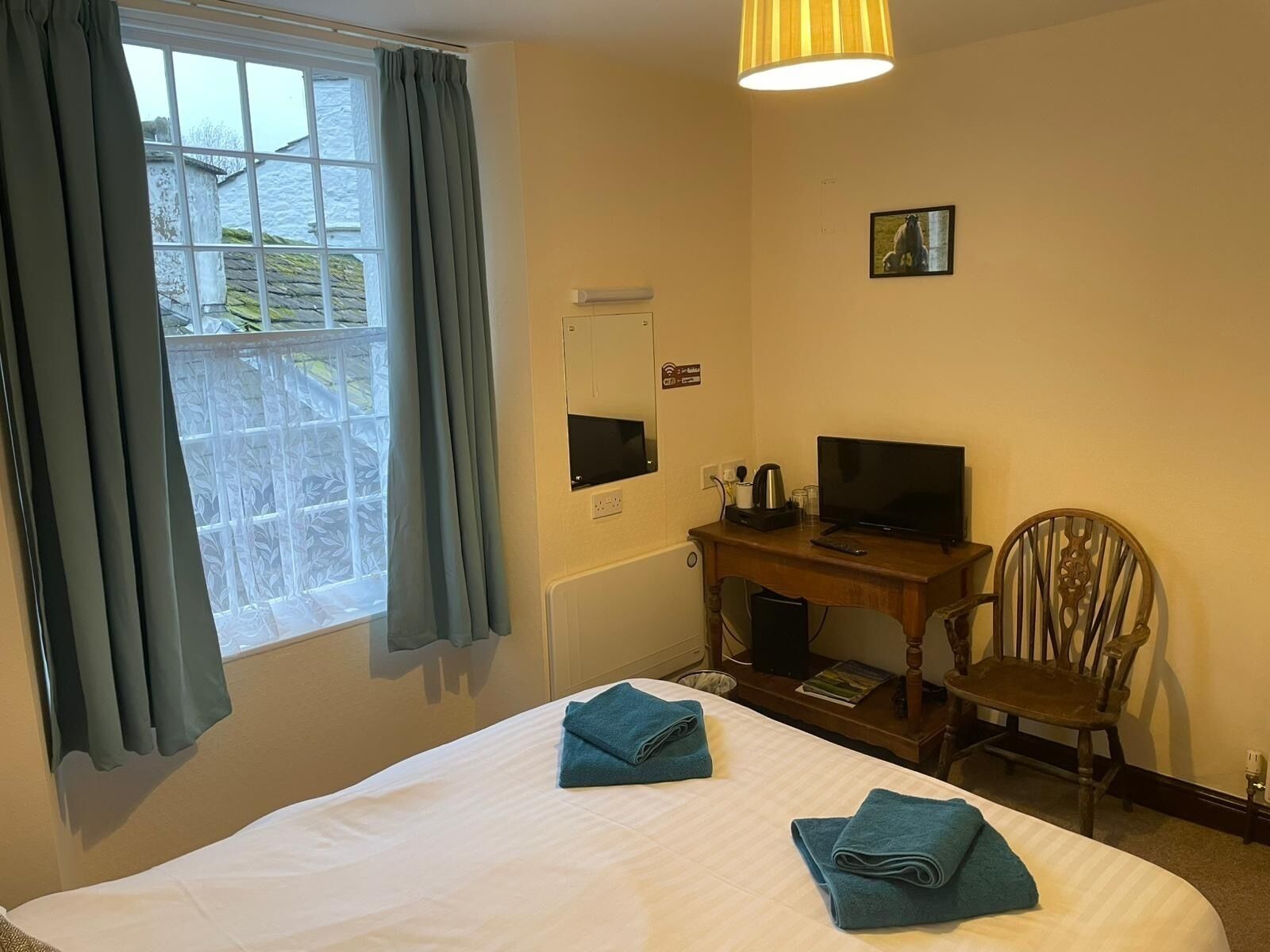 A hotel room with a bed, a desk with a computer, a chair, and a window with curtains.