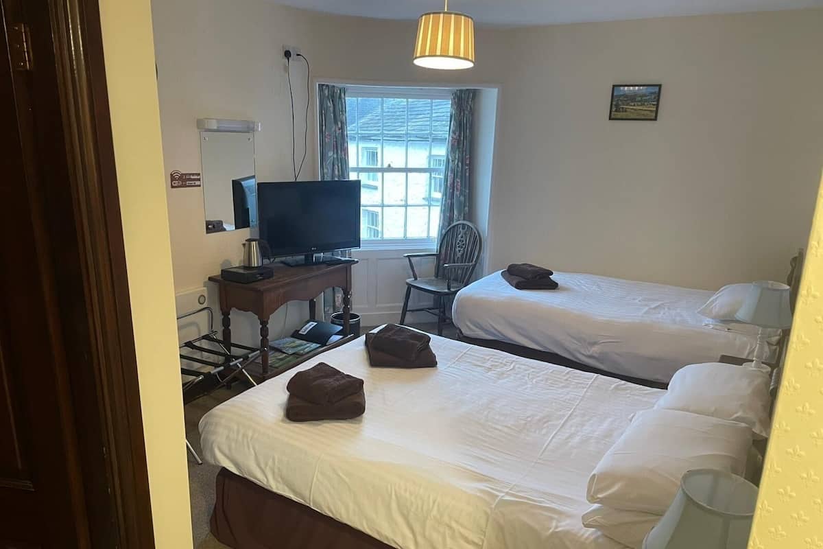 A hotel room with two beds, a TV, a desk with a computer, a chair, and a window with curtains.