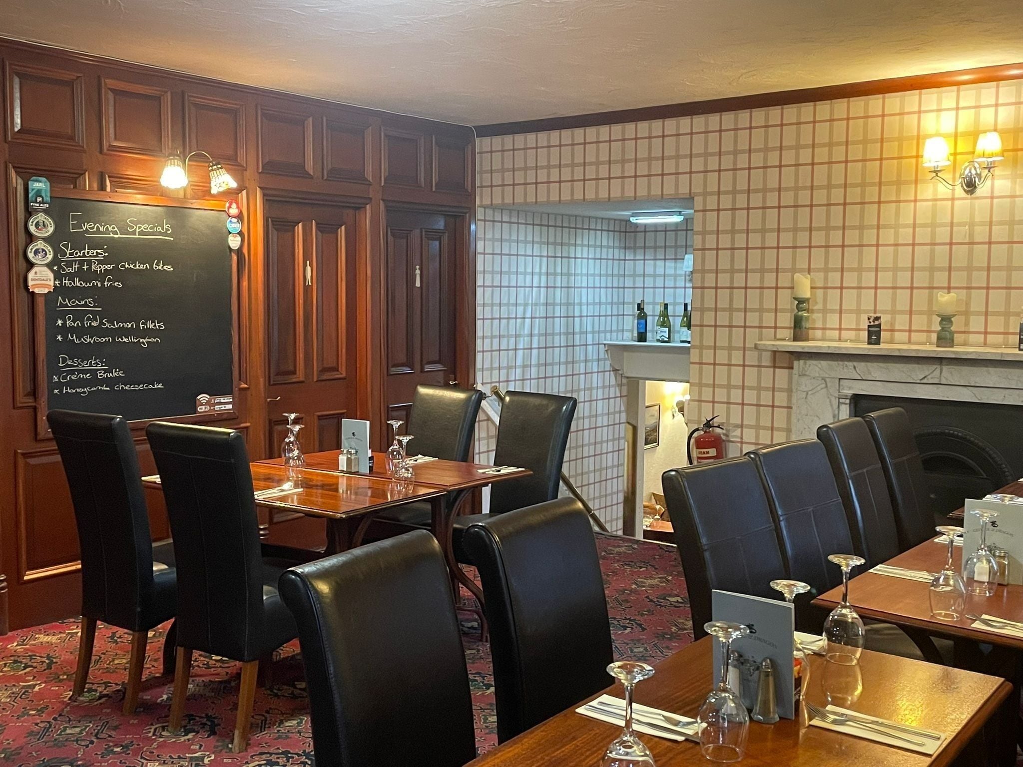 A restaurant with a blackboard menu, wooden paneling, and a fireplace.