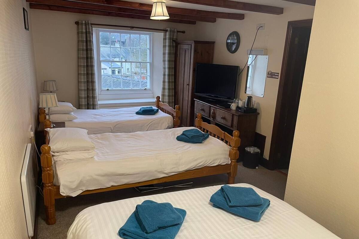 A hotel room with two wooden beds, a television, a window with curtains, and a wall clock.